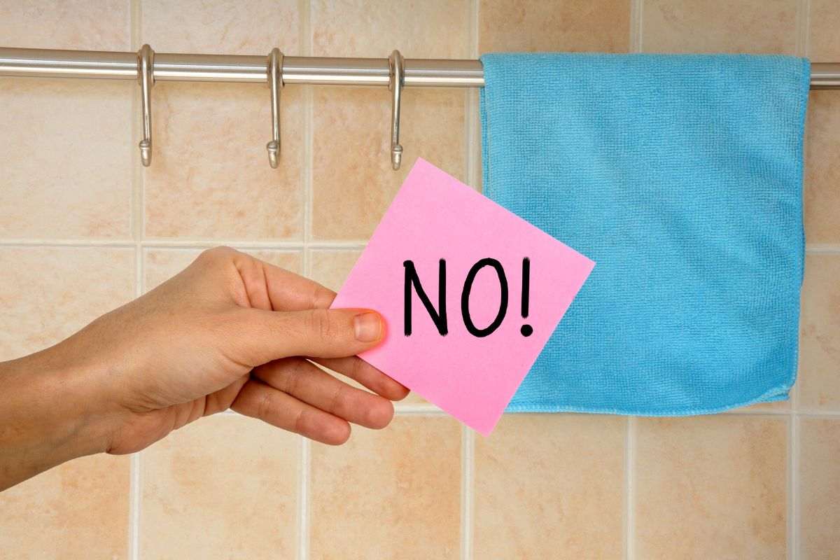 strofinaccio appeso in cucina e mano che mantiene un post-it con scritto no