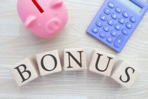 scritta bonus con accanto calcolatrice viola e maialino salvadanaio rosa