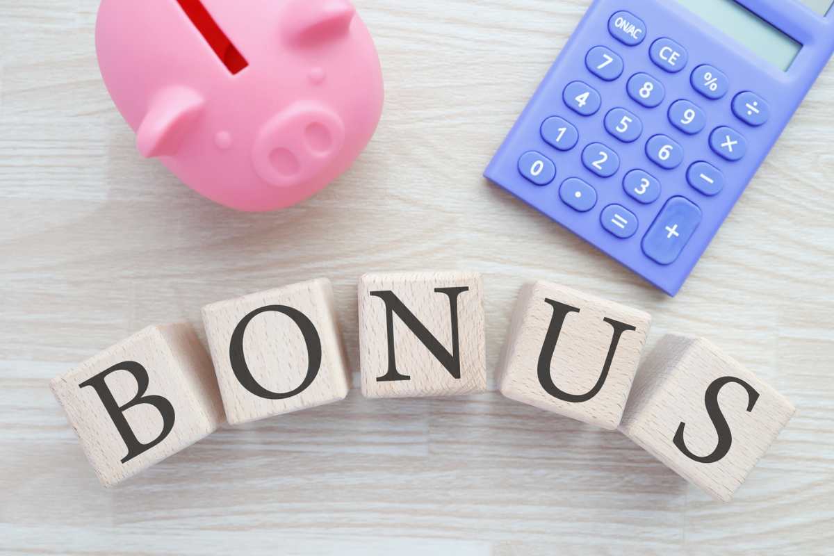 scritta bonus con accanto calcolatrice viola e maialino salvadanaio rosa 