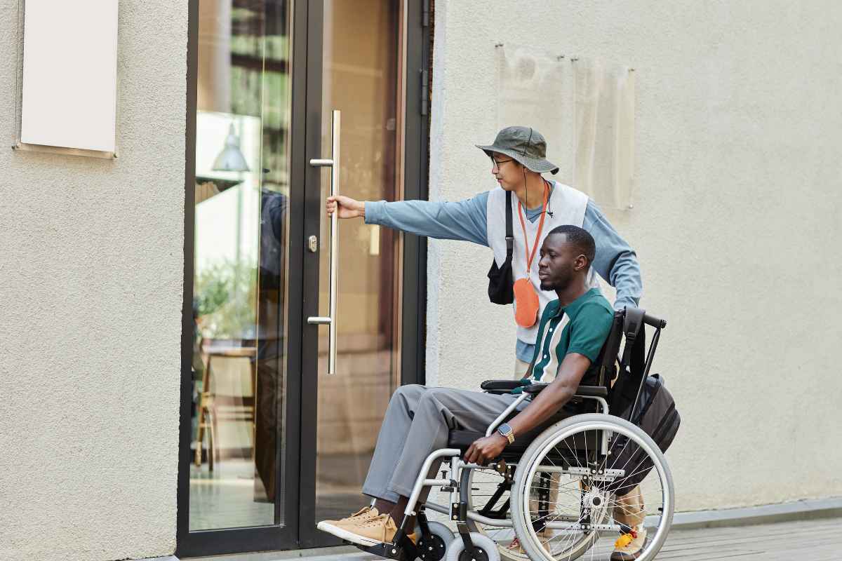 persona in carrozzina che entra in un palazzo con il suo caregiver