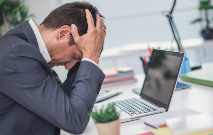 uomo preoccupato con la testa tra le mani seduto davanti al computer