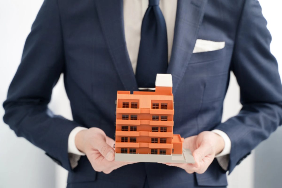 uomo con in mano un condominio in miniatura