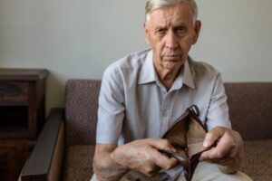 uomo anziano seduto sul divano che mostra un portafoglio vuoto
